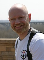 John in a white t-shirt and black leather vest, smiling at the camera